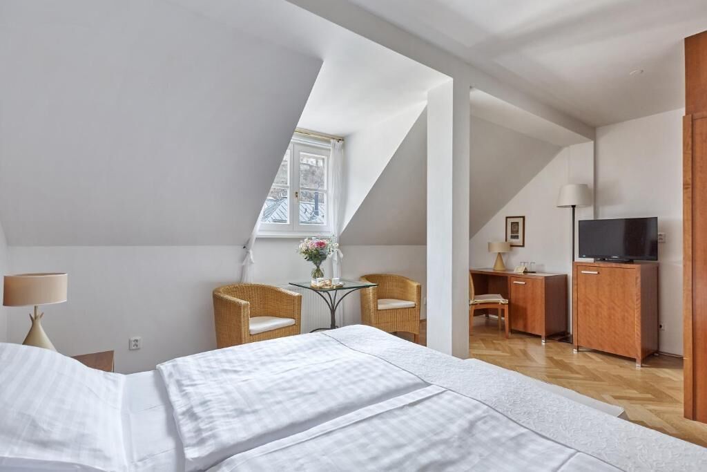 A bedroom with a bed, a desk, a television, and a window.