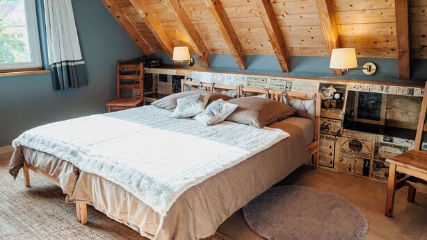 A bedroom with a large bed, wooden ceiling beams, two wall-mounted lamps, and a window with curtains. - NEW ACCOMMODATIONS IN A VILLAGE HOUSE (Orschwiller)