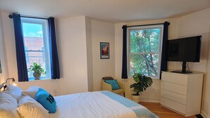 A bedroom with a bed, a television, a dresser, and two windows with curtains. - 2-bedroom Rowhome w/ AC in South Philly 10 min to Plane/Train & 5 min to Stadium (Philadelphia)