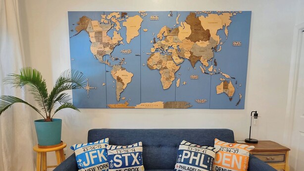 A living room with a blue sofa, a world map on the wall, and decorative pillows with city names. - 2-bedroom Rowhome w/ AC in South Philly 10 min to Plane/Train & 5 min to Stadium (Philadelphia)