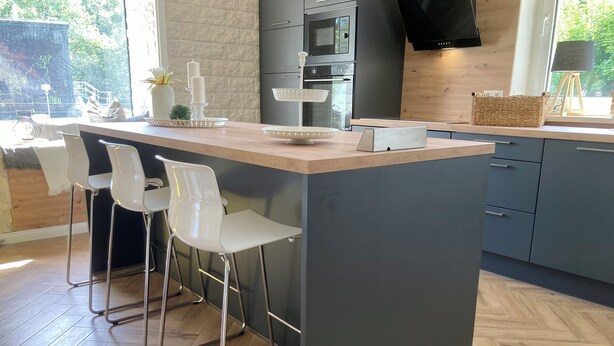 Una cocina moderna con una isla central, taburetes de bar, horno empotrado y un ventanal amplio.