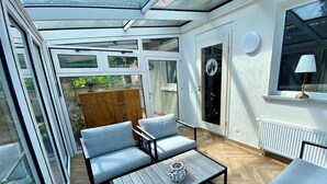 Un patio luminoso con techo de vidrio, una mesa de madera y dos sillas acolchadas.