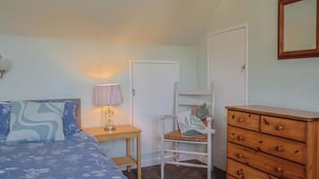 Un dormitorio con cama, una silla, cómoda, lámpara y una puerta.