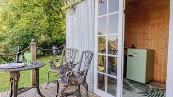 Una terraza de madera con una mesa y sillas, un refrigerador verde y una puerta corrediza de vidrio a una habitación.