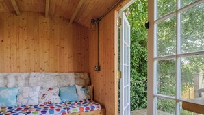 A wooden cabin with a bed, a window, and a view of greenery. - Tane (Blandford Forum)