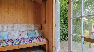 A wooden cabin with a bed, a window, and a view of greenery.
