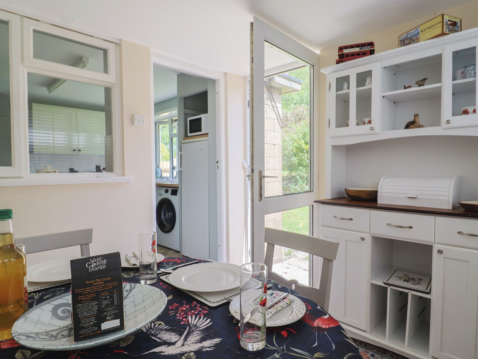 A dining area with a table set for two, a microwave in the background, and a view of the outside.