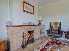 Un salón con chimenea de piedra, un sillón de cuero, un cuadro en la pared y una alfombra estampada.