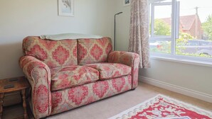 A room with a patterned sofa, a framed picture on the wall, a floor lamp, and a window with curtains. - Tane (Blandford Forum)