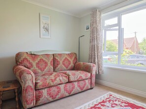 A room with a patterned sofa, a framed picture on the wall, a floor lamp, and a window with curtains. - Tane (Blandford Forum)