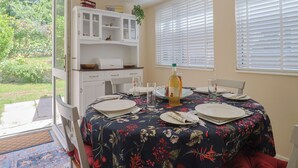 A dining area with a table set for four, a white cabinet with glass doors, and a view of greenery outside. - Tane (Blandford Forum)
