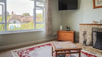 A living room with a fireplace, a television mounted on the wall, a window with a view of houses, and a small table with magazines.