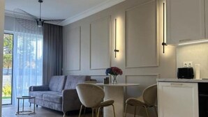 A modern living room with a sofa, chairs, a coffee table, and a kitchen area with cabinets and a countertop. - Let's Sea SPA - Premium Apartamenty  (Gąski)