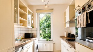 A compact kitchen with a washing machine, a microwave, and a window with a view of greenery.