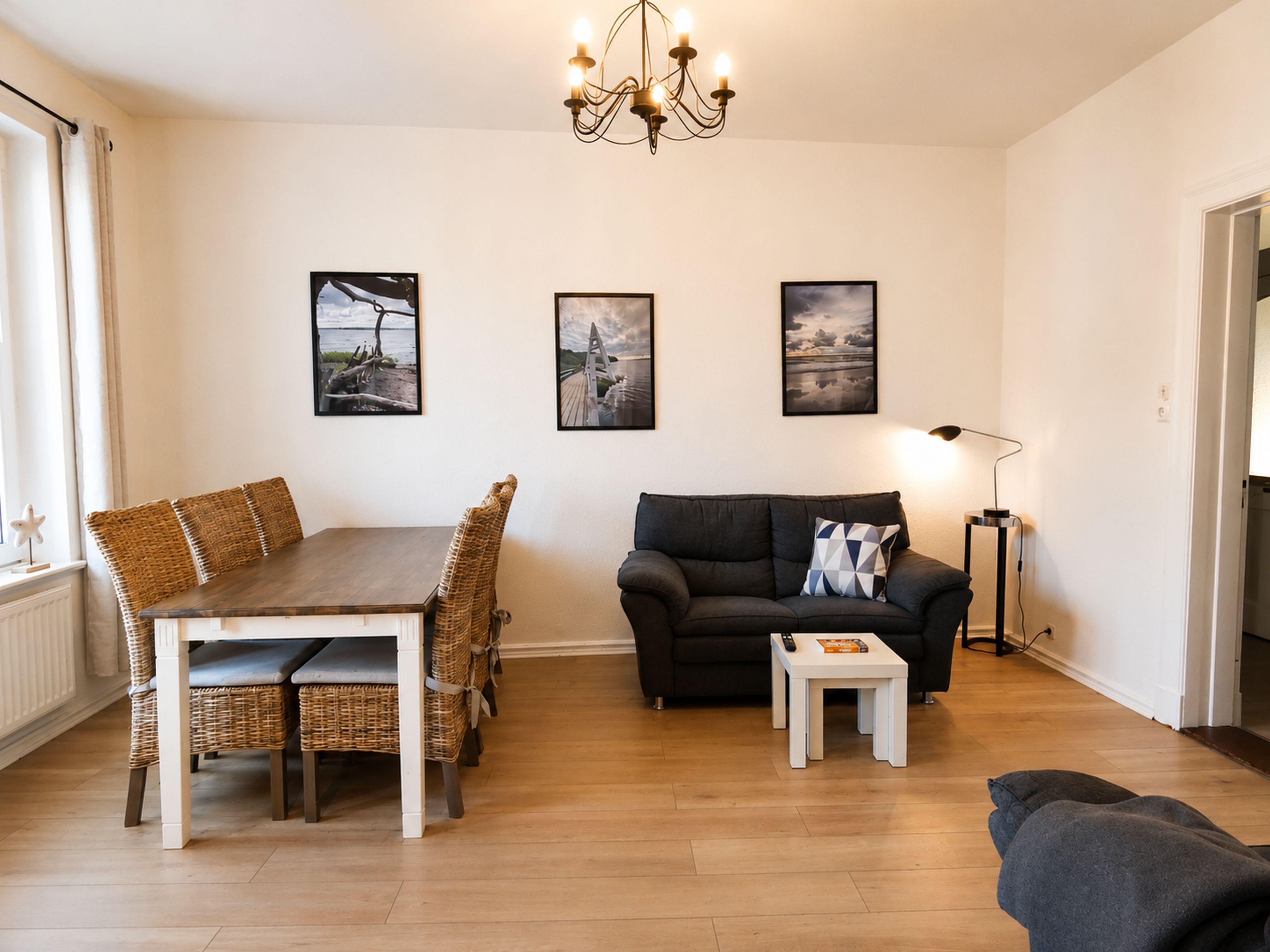 A living room with a dining table, a sofa, a small coffee table, and a lamp. There are three framed pictures on the wall.