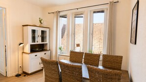 A dining area with wicker chairs, a white cabinet, and a window with curtains.