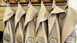 Een rek met beige badjassen met geborduurde logo's, aan een houten wand.