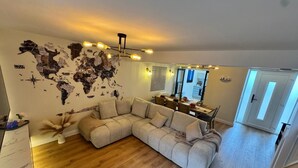 Een woonkamer met een modulaire bank, een wereldkaart op de muur, een eethoek met een tafel en stoelen, en een keuken op de achtergrond.