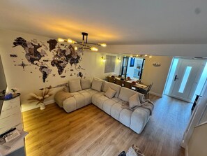 A living room with a sectional sofa, a world map wall, a dining area with a table and chairs, and a kitchen in the background. - Posh 3-BDR Home, Beach House - Sleep6 - WiFi - Hot Tub - Free On-Street Parking (Donaghadee)