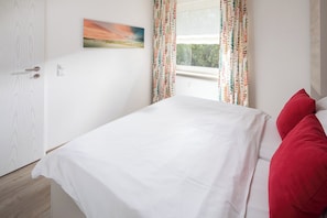 Ein Schlafzimmer mit einem Bett, einer Tür, einem Fenster und einem Bild an der Wand.