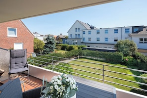Ein Balkon mit Blick auf ein Wohngebiet, darunter ein Backsteinhaus und ein weißes Gebäude mit vielen Fenstern.