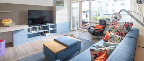 Ein modernes Wohnzimmer mit Flachbildfernseher, einer Couch, einem Couchtisch und einem Bücherregal.