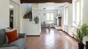 Amplia sala de estar con una escalera, una mesa de comedor con sillas y un sofá con un cojín.