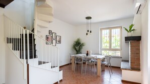 Un comedor con una mesa, sillas, una escalera y una ventana con una planta.