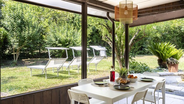 Un patio al aire libre con una mesa lista para comer, rodeada de sillas y un colgante de luz.