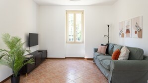 Una sala de estar con televisor, sofá, ventana y planta.