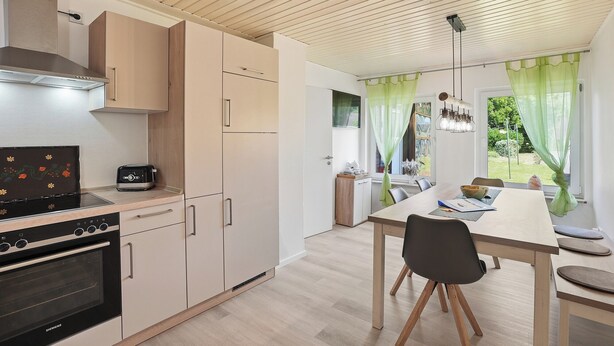 Une cuisine moderne dotée d’un four encastré, un coin repas avec une table et des chaises, et une vue sur l’extérieur par une fenêtre.