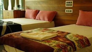 Habitación de hotel con dos camas, cabecero de madera, una mesita con lámpara y ventana con cortinas.