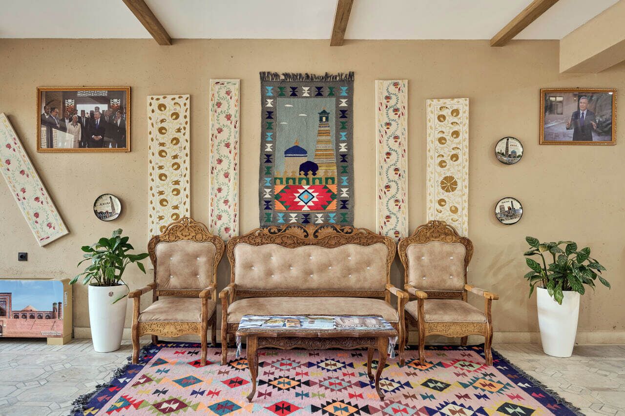 A room with a sofa set, two potted plants, a patterned rug, and decorative wall hangings.