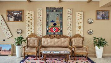 A room with a sofa set, two potted plants, a patterned rug, and decorative wall hangings.