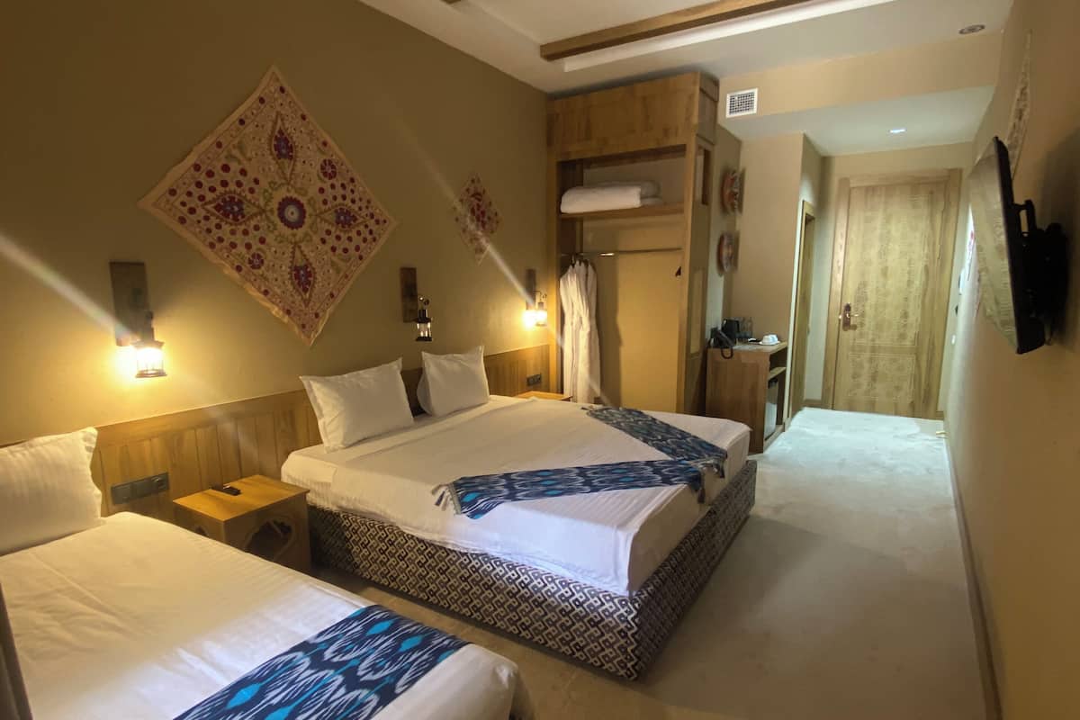 Quarto de hotel com duas camas, teto de madeira, televisão fixada na parede e corredor que leva a outro quarto.