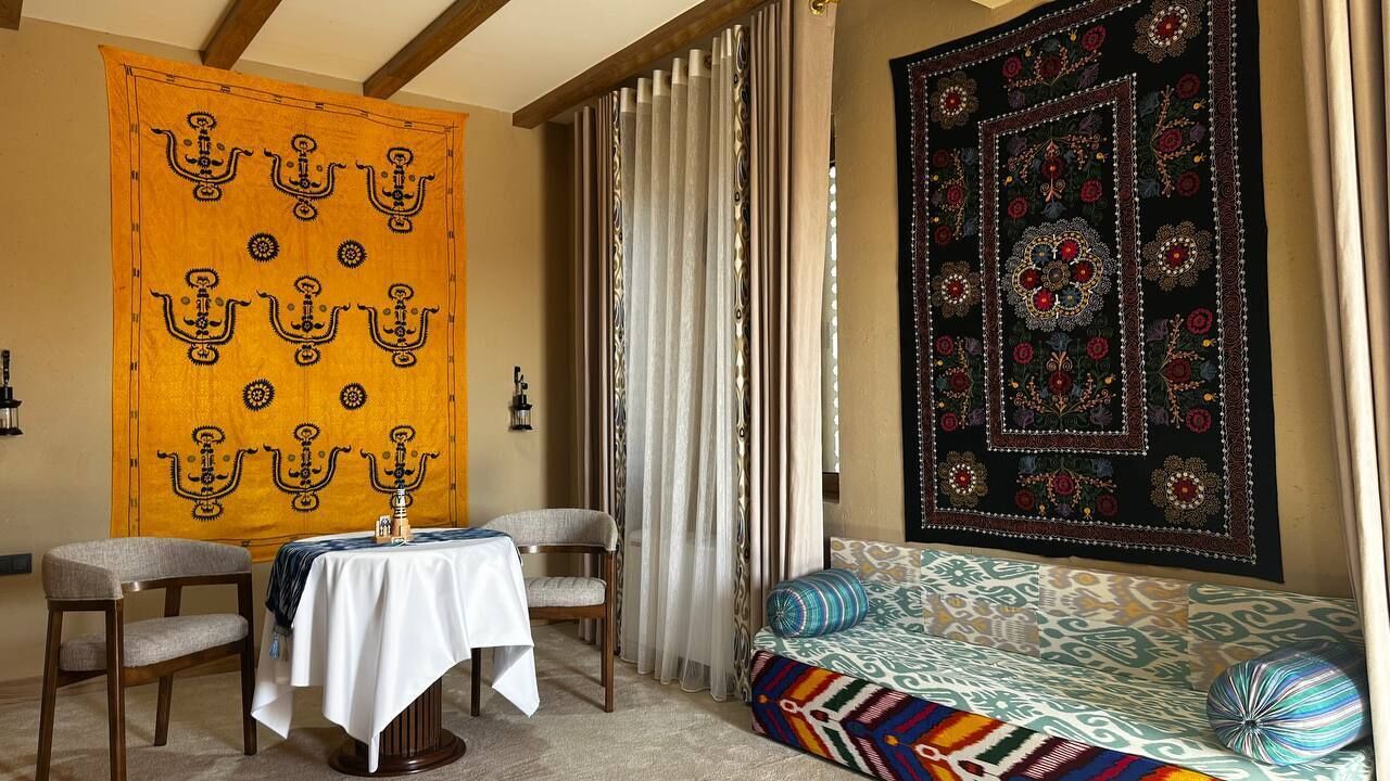 Una habitación con un tapiz estampado, un sofá con cojines, una mesa con mantel blanco y dos sillas.