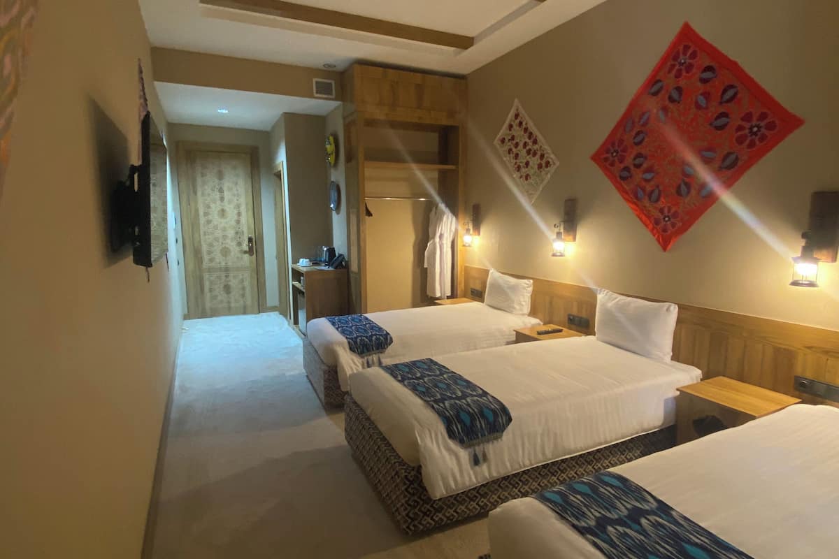 Quarto de hotel com duas camas, teto de madeira, tapeçaria vermelha e corredor que dá para um banheiro.