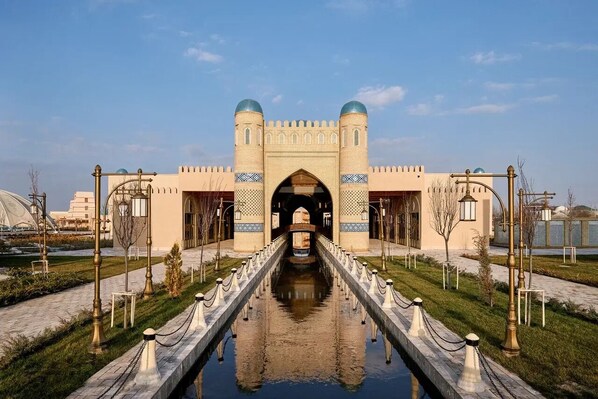 A historic building with a central archway, a reflective waterway, and a symmetrical design. - Arda Karvon Saroy (Khiva)