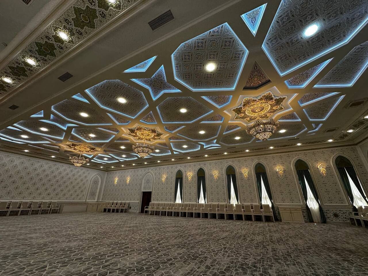 A large hall with patterned walls, star-shaped ceiling lights, and arched windows.
