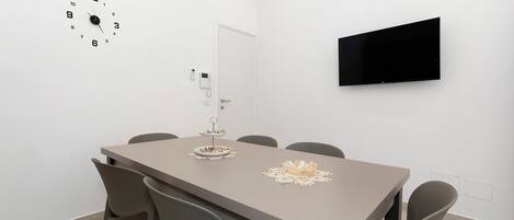 Uma sala de conferências com uma mesa, cadeiras, um relógio, uma porta e uma TV fixada na parede.