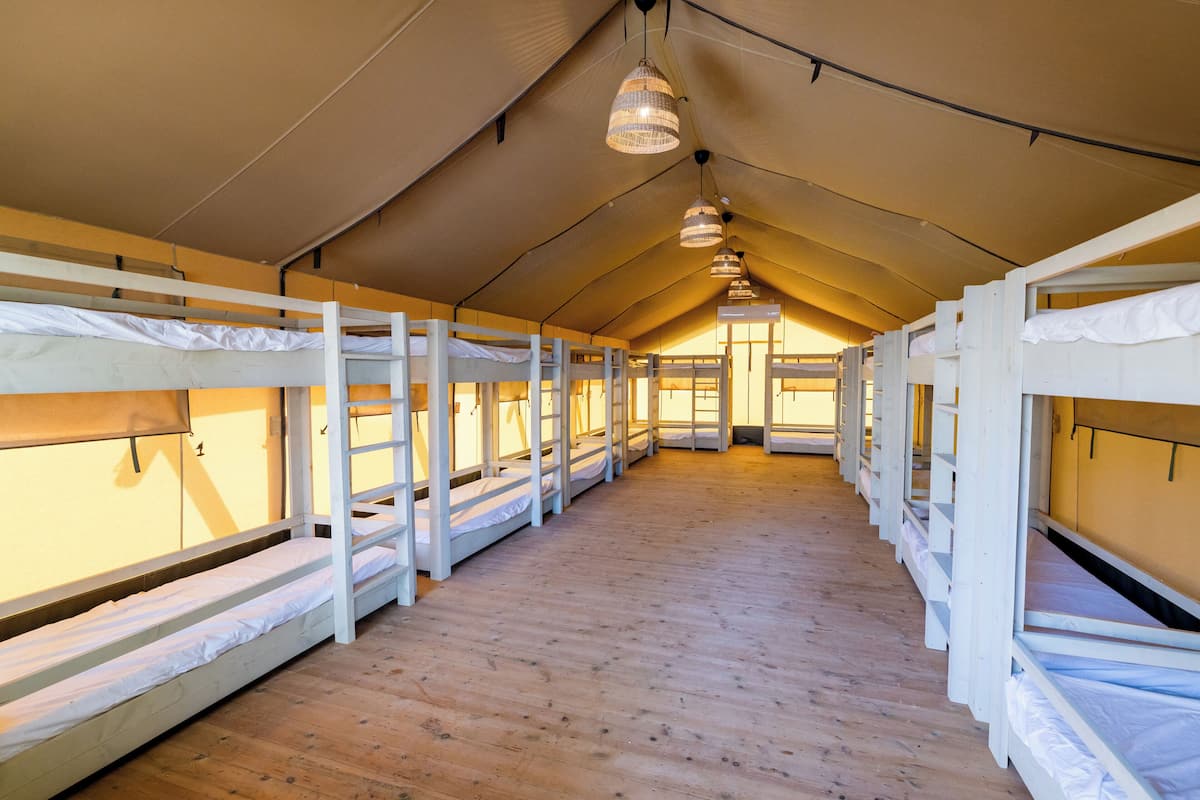 En rad med våningssängar placerade under ett tältliknande tak, med ett trägolv.