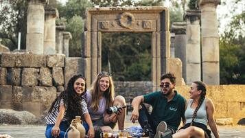 A group of people sitting on a wooden deck with stone ruins in the background.