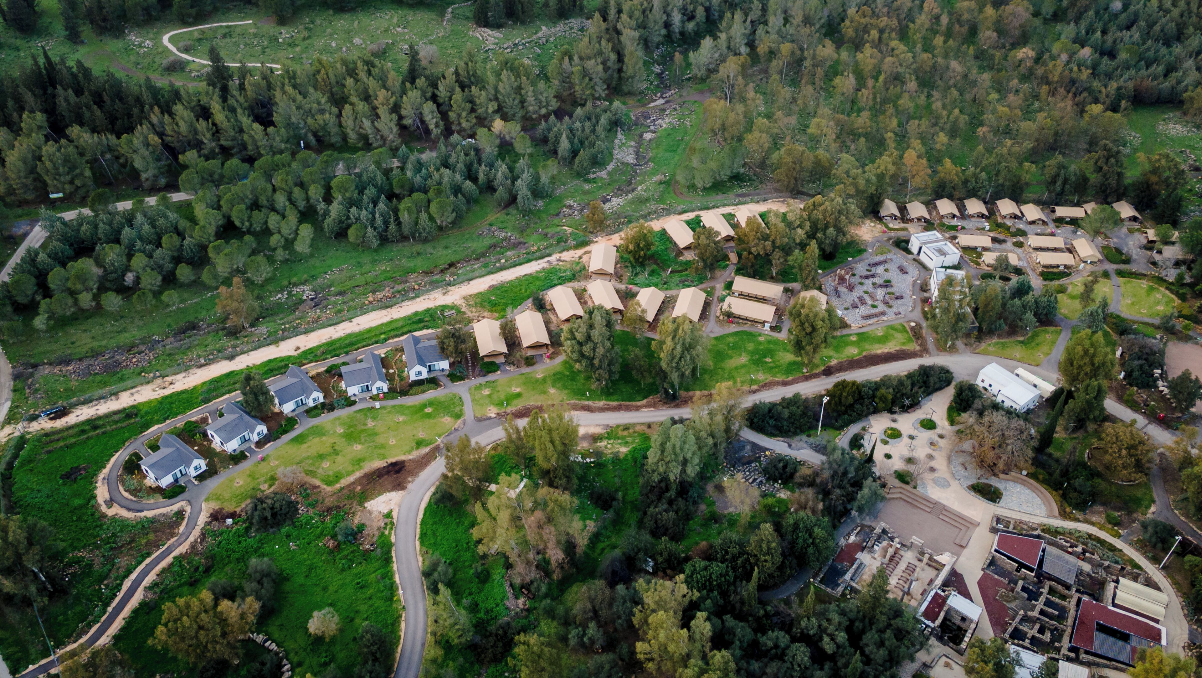 Een luchtbeeld van een camping met meerdere tentaccommodaties in rijen, omgeven door dicht bos.