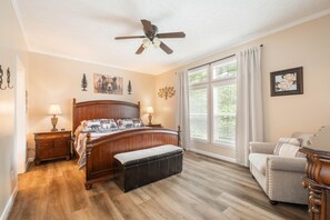 Ein Schlafzimmer mit einem hölzernen Bett, einer Bank, einem Sessel, einem Deckenventilator und einem Fenster mit Jalousien.