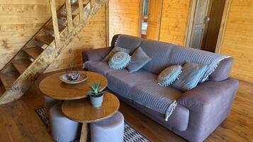 Ein Holzinnenraum mit einer Couch, Poufs, einem runden Tisch und einer Treppe.