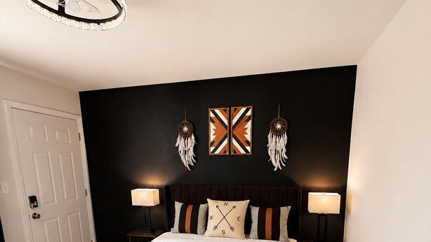 A bedroom with a bed, two bedside tables, a wall-mounted lamp, a ceiling light fixture, and a door.