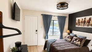 Ein Schlafzimmer mit einem Bett, einem Schreibtisch, einer Kaffeemaschine, einem Fernseher und einem Fenster mit Vorhängen.