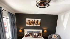 Ein Schlafzimmer mit einem Bett, einem Sessel, einer Lampe, einem Gemälde und einer Deckenleuchte.