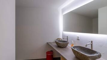 Un baño moderno con dos lavamanos de piedra, un cubo de basura rojo y un espejo grande.