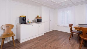 Une cuisine avec des meubles blancs, un four à micro-ondes, une machine à café et un coin repas comprenant une table et des chaises en bois.